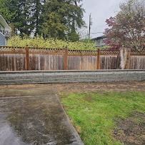 Low grey block retaining wall with lattice privacy fence behind a lawn