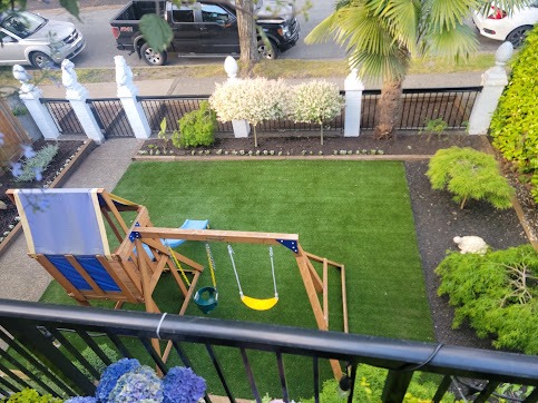 Family backyard with artificial turf, playset, and mulched planting beds