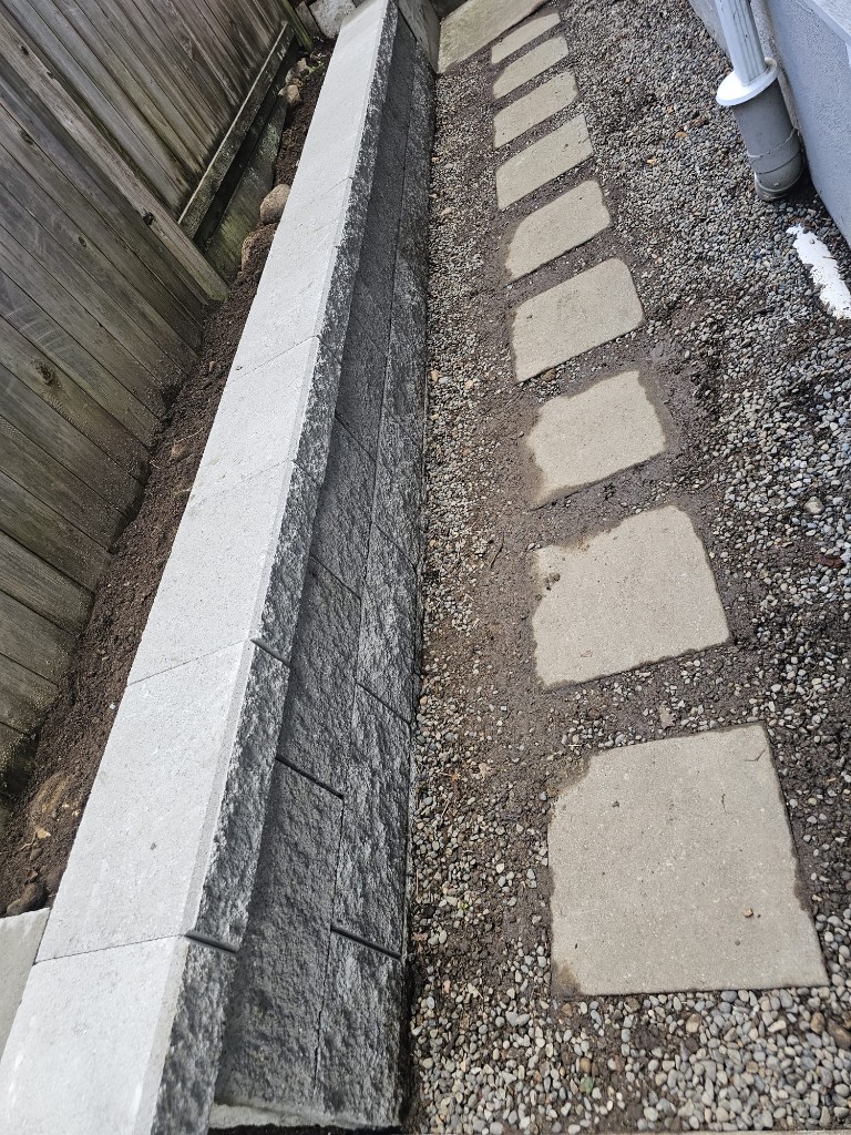 New block retaining wall beside a gravel path with square stepping stones