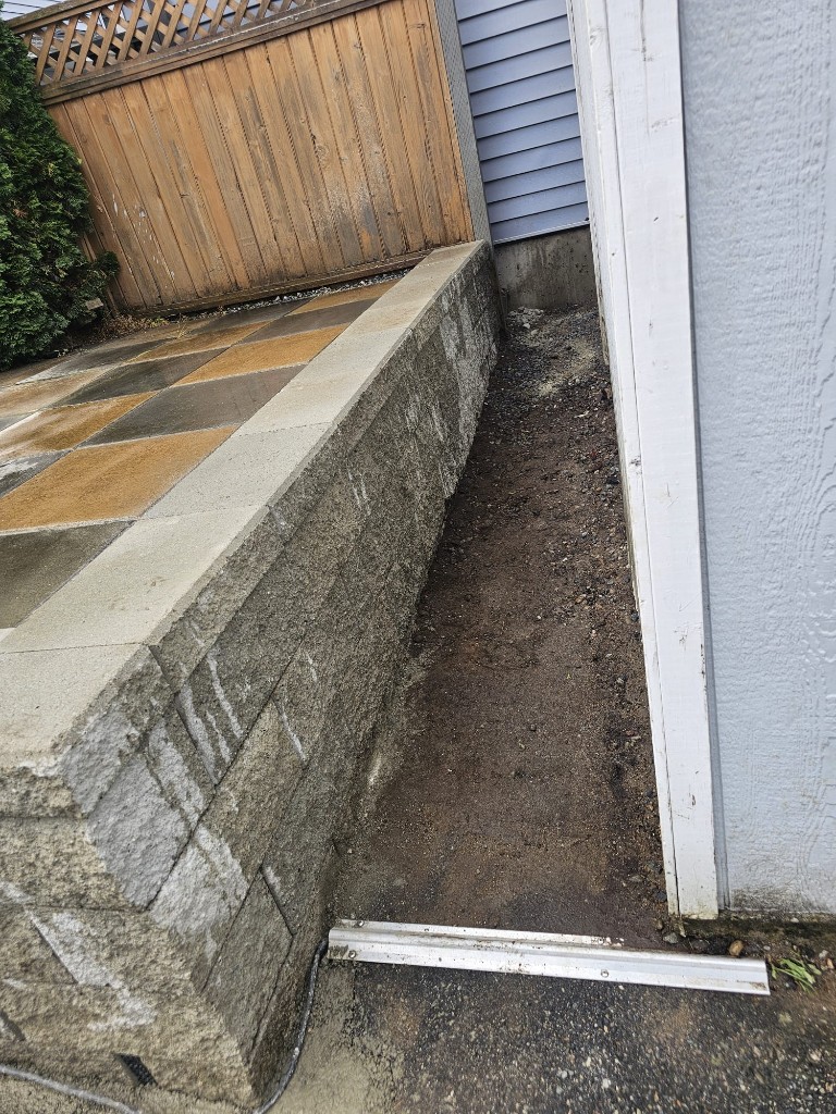 Concrete block retaining wall supporting a checkerboard paver patio beside a house