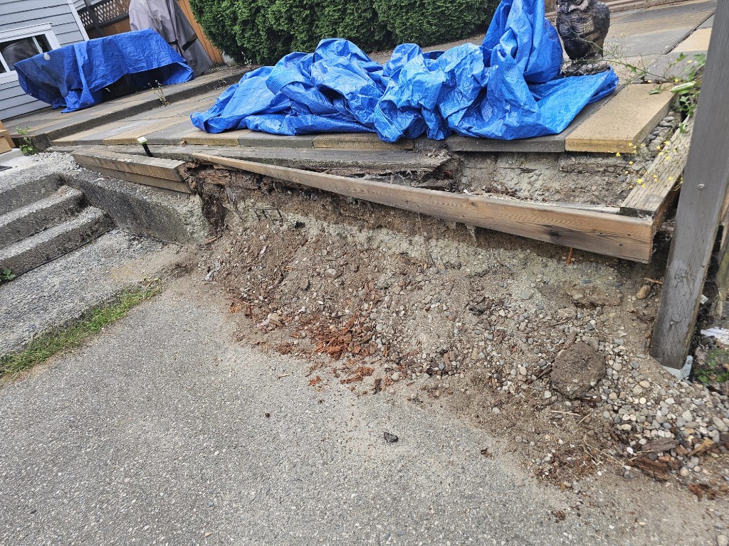 Collapsed timber retaining wall with soil spilled onto the driveway